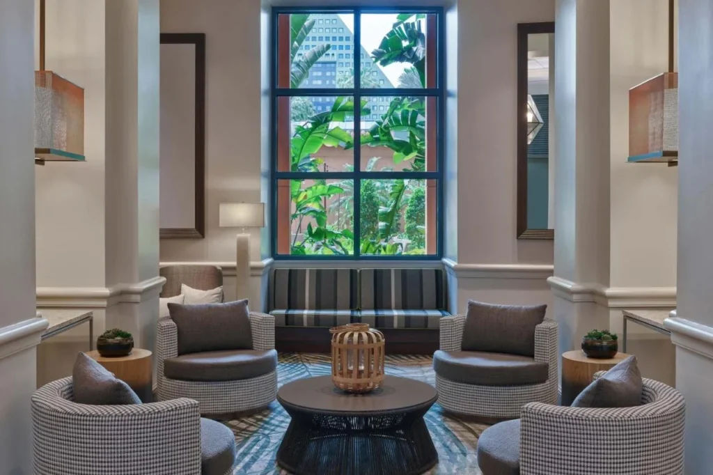 Lobby lounge with gray armchairs and a tall window facing tropical plants, Walt Disney World Swan