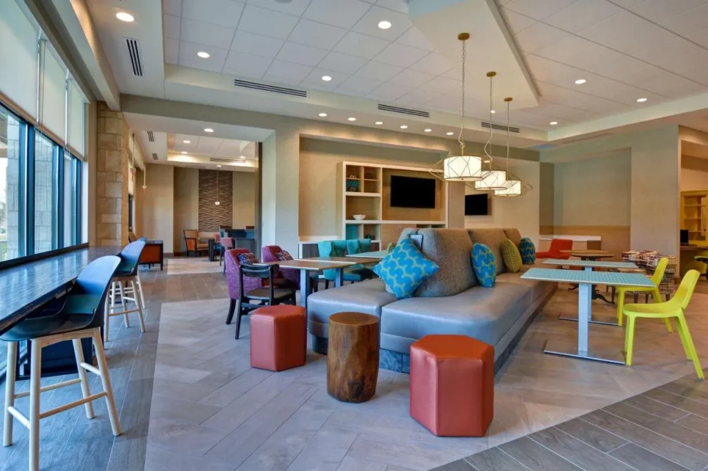 Salón del vestíbulo con sofá gris, taburetes coloridos y mostrador de la ventana en Home2 Suites Flamingo Crossings