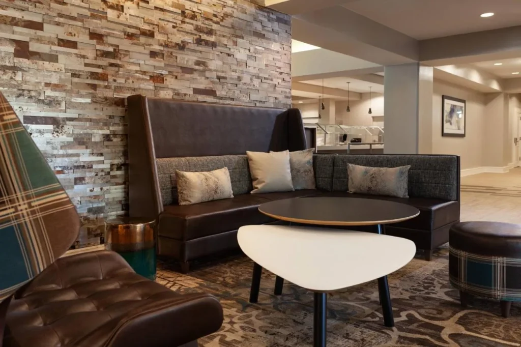 Salón del vestíbulo con banqueta de cuero, pared de piedra y mesas bajas en el Residence Inn Orlando at SeaWorld