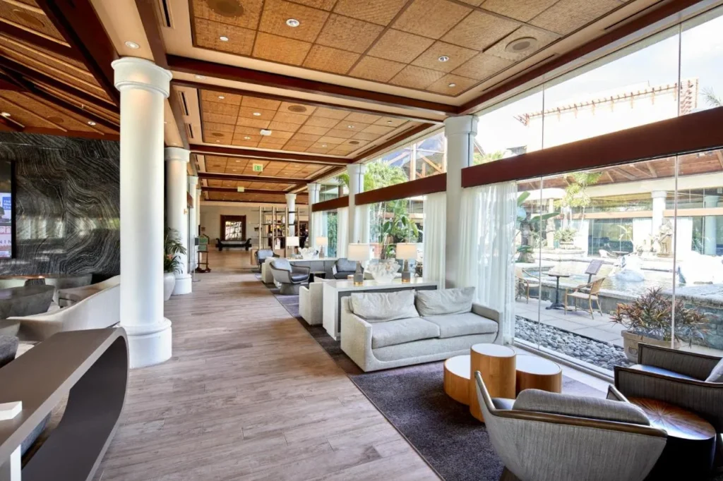 Sal&oacute;n del vest&iacute;bulo con sof&aacute;s y ventanas de piso a techo hacia el patio en Loews Royal Pacific Resort
