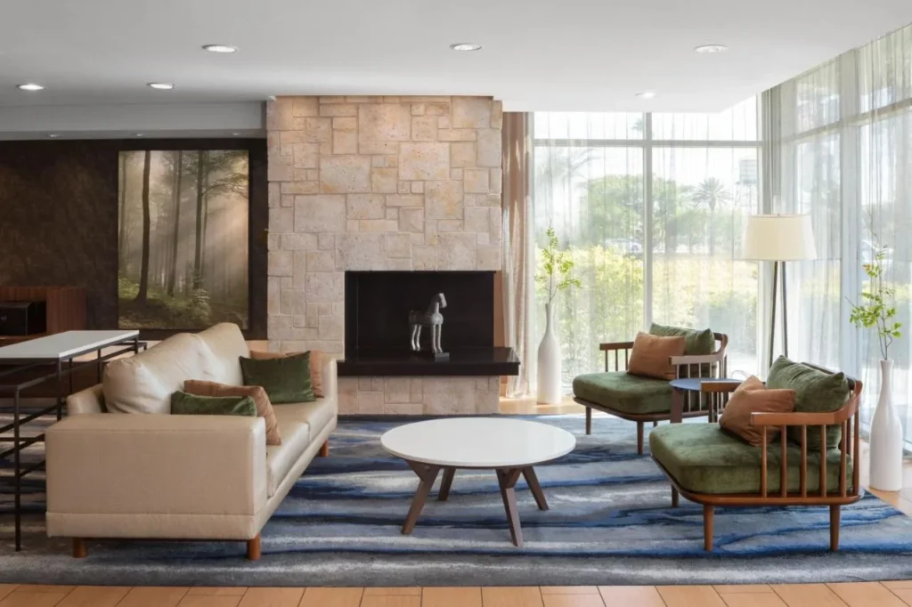Salón en el vestíbulo con chimenea de piedra, sofá y sillones verdes en Fairfield Inn & Suites Orlando Kissimmee/Celebration