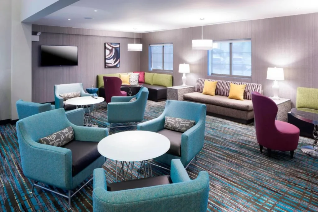 Sal&oacute;n del vest&iacute;bulo con sillones color verde azulado, mesas redondas y sof&aacute;s en el Residence Inn Near Universal Orlando