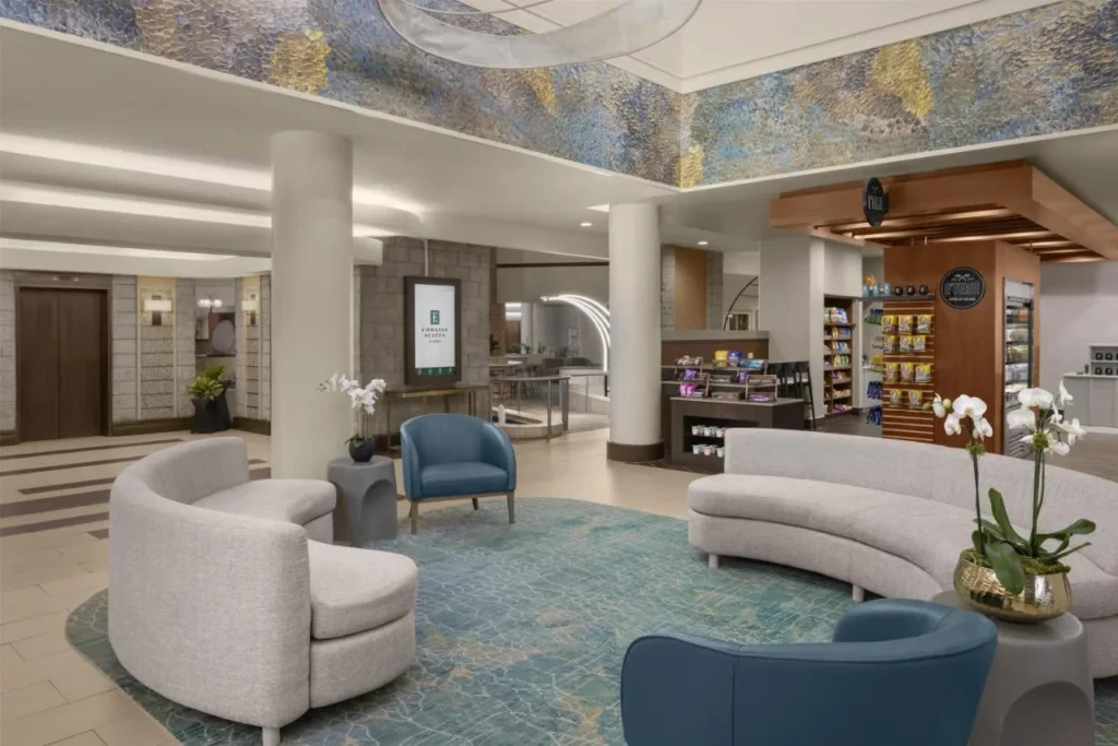 &Aacute;rea de asientos en el vest&iacute;bulo con sof&aacute;s curvos junto al mercado de E'terie en Embassy Suites ICON Park