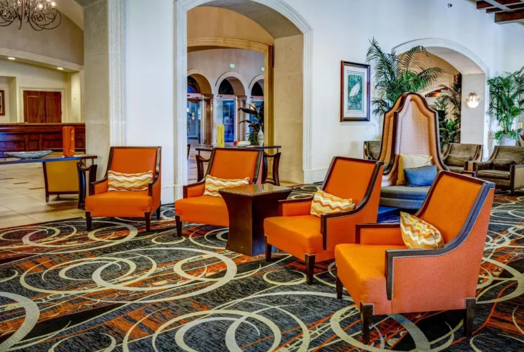 Lobby seating area with orange armchairs, swirl-pattern carpet and arched doorways at Rosen Shingle Creek