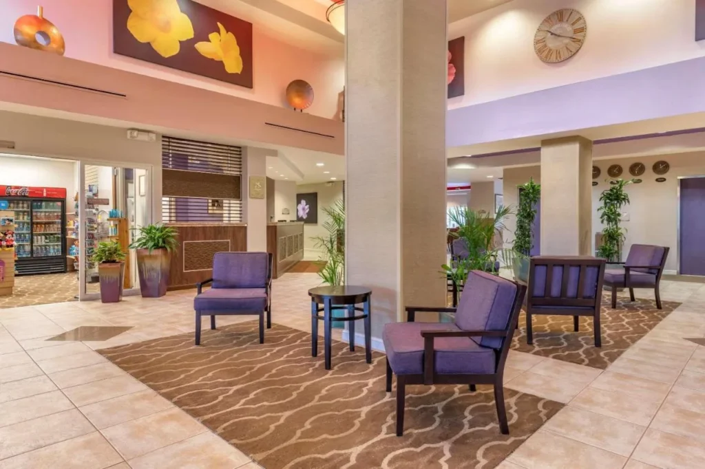 Zona de asientos en el vest&iacute;bulo con sillas moradas junto a la tienda de art&iacute;culos varios en Comfort Suites Maingate East