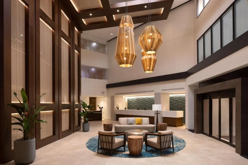 Vest&iacute;bulo con paneles de madera altos, luces colgantes tejidas y recepci&oacute;n en DoubleTree Suites Disney Springs