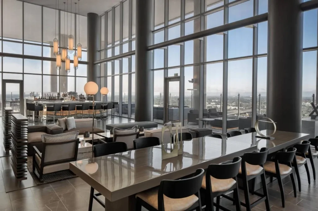 Mesa de comedor larga y bar interior junto a las ventanas del piso al techo en AC Hotel Orlando Downtown