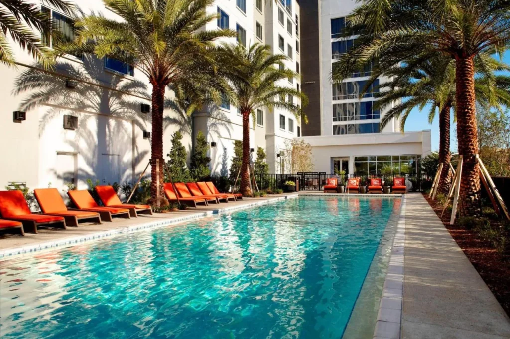 Piscina exterior larga con tumbonas naranjas y palmeras en el Residence Inn Orlando Lake Nona