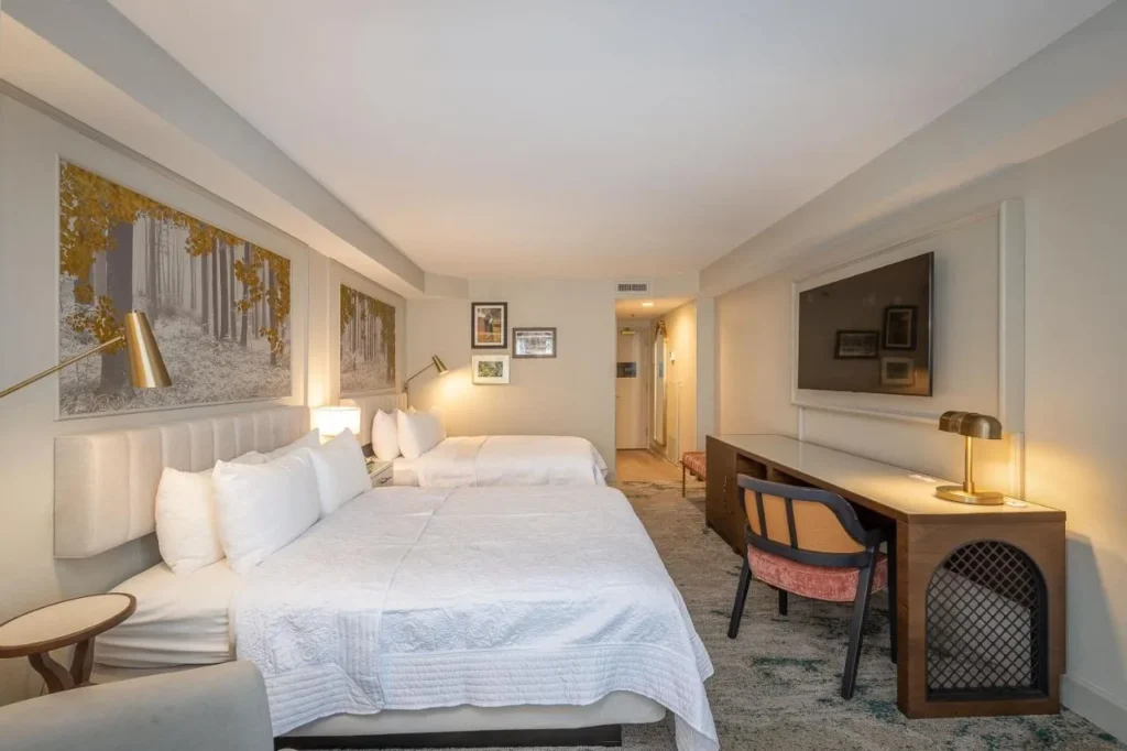 Long two-queen room with a desk, wall TV and forest murals at Castle Hotel Orlando