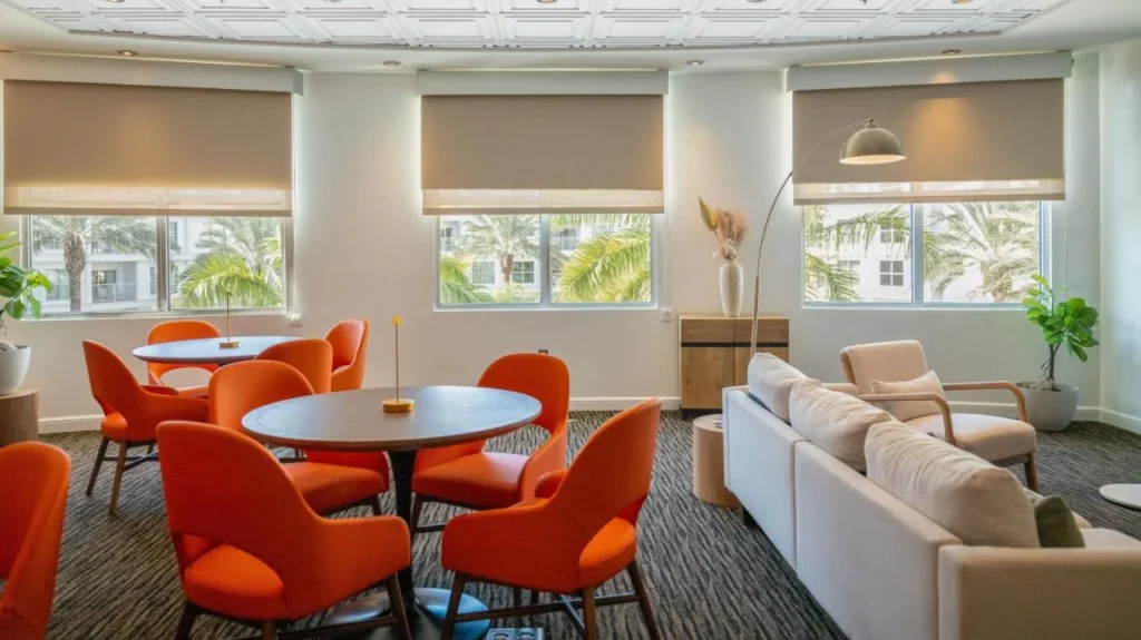 Salón con sillas naranjas, mesas redondas y ventanas con vista de palma en Meliá Orlando Celebration