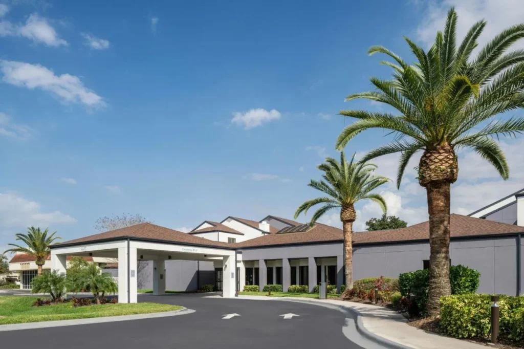 Low-rise entrance canopy, driveway and tall palm trees at Courtyard by Marriott Orlando Airport