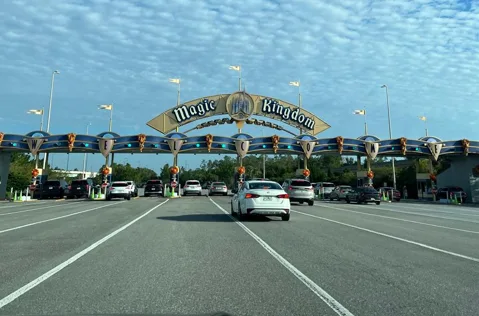 Coches que se acercan a la plaza de peaje de Magic Kingdom debajo de su gran letrero del arco de entrada