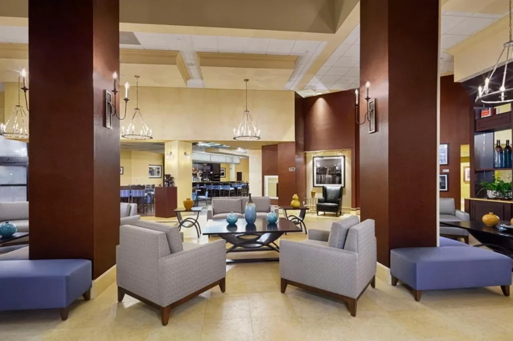 Vest&iacute;bulo principal con sillones grises, columnas de madera y candelabros en DoubleTree by Hilton Orlando Downtown
