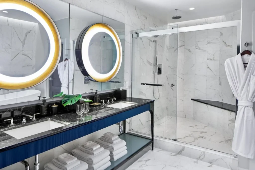 Marble bathroom with double vanity, round lit mirrors and walk-in shower at Hotel Beauden