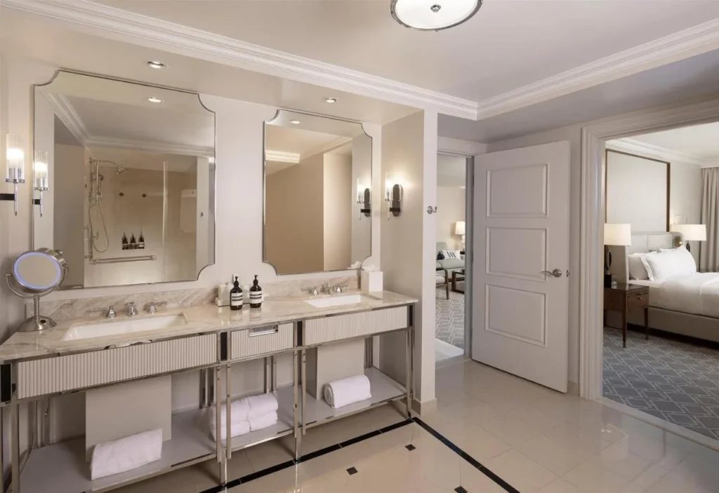 Doble tocador de mármol en un baño Waldorf Astoria Orlando suite, con el dormitorio a través de la puerta