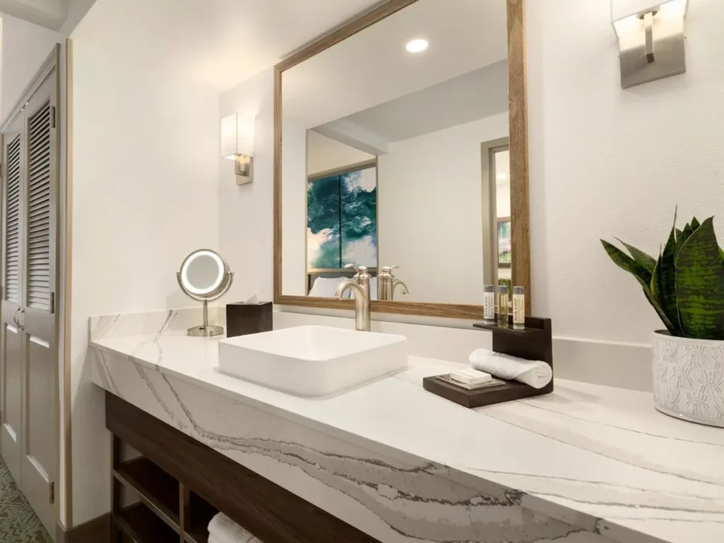 Marble-look vanity with a vessel sink, mirror and sconces at Buena Vista Suites Orlando