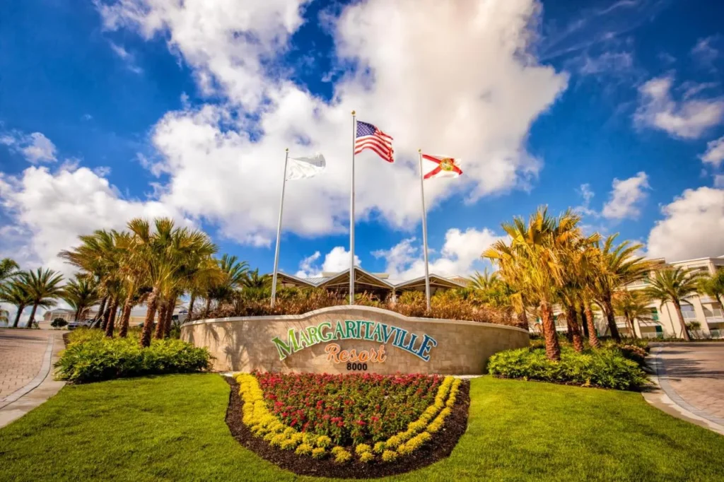 Margaritaville Resort Orlando entrance sign with a flower bed, palm trees and three flagpoles