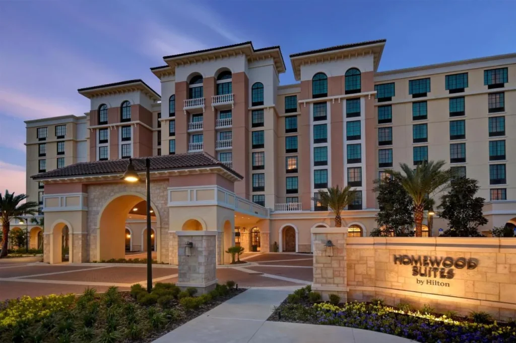 Entrada de estilo mediterr&aacute;neo y se&ntilde;al de piedra de Homewood Suites by Hilton Orlando at Flamingo Crossings en el crep&uacute;sculo