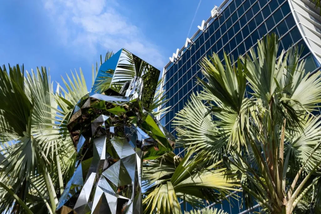 Escultura geom&eacute;trica reflejada y palmeras frente a la torre del Lake Nona Wave Hotel