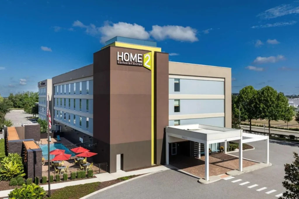 Modern exterior, covered entrance and fenced pool with red umbrellas at Home2 Suites by Hilton Clermont