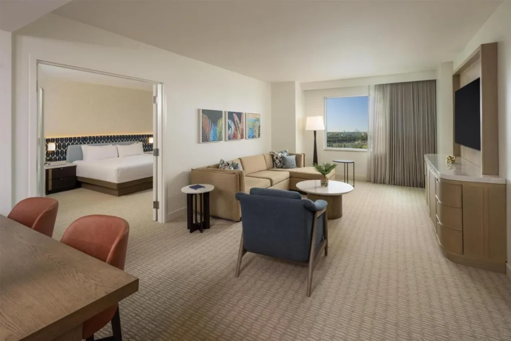 Suite de un dormitorio en Hilton Orlando con un dormitorio king m&aacute;s all&aacute; de un sof&aacute; seccional y mesa de comedor