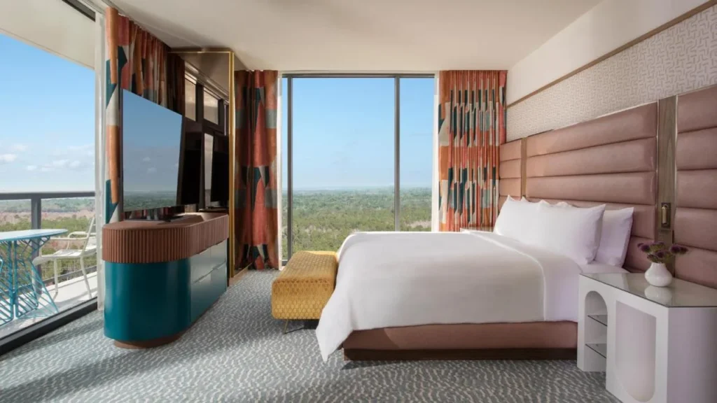 Suite de un dormitorio con cabecera rosa, balc&oacute;n y ventanas de piso a techo en Lake Nona Wave Hotel