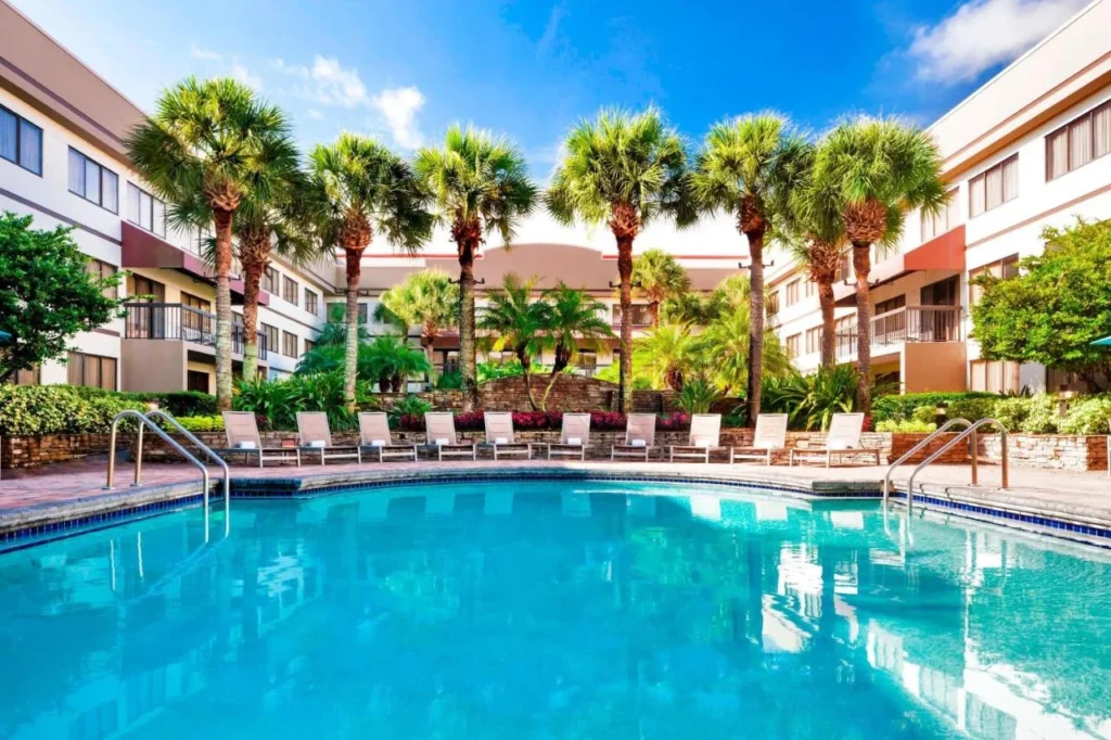 Open-air courtyard pool with palm trees and lounge chairs between the guest wings at Sheraton Suites Orlando Airport