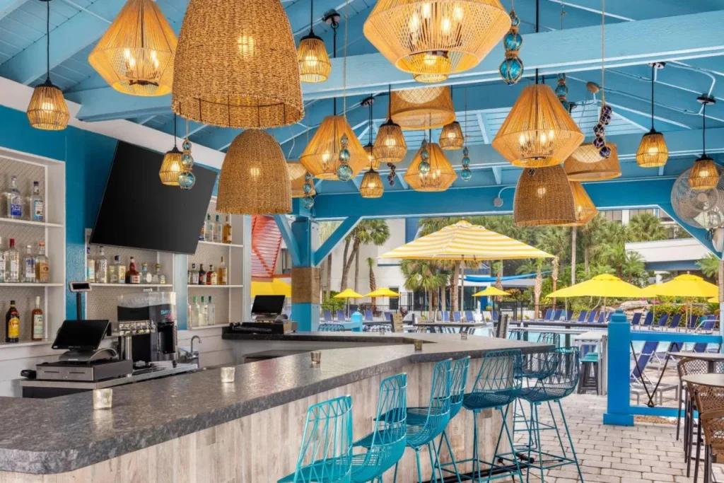 Barra de piscina al aire libre con l&aacute;mparas de mimbre y taburetes turquesas en Delta Hotels Orlando Celebration