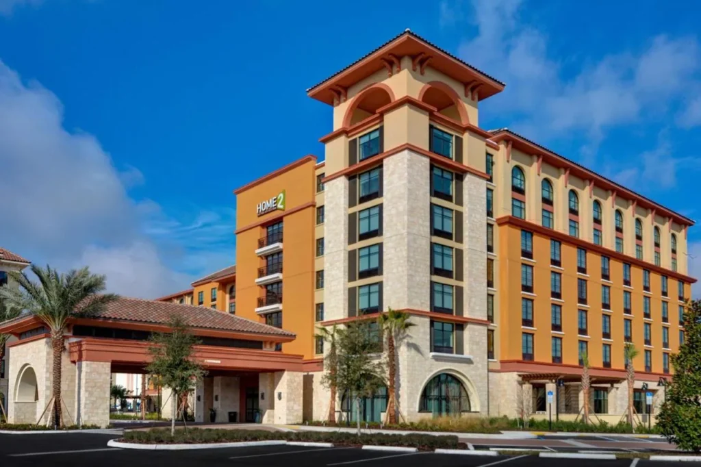 Torre de hotel de color naranja y piedra con entrada cubierta en Home2 Suites Orlando Flamingo Crossings