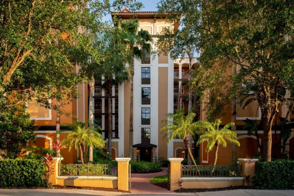 Edificio de condominios naranja con balcones detrás de los árboles y una pasarela cerrada en Floridays Resort Orlando
