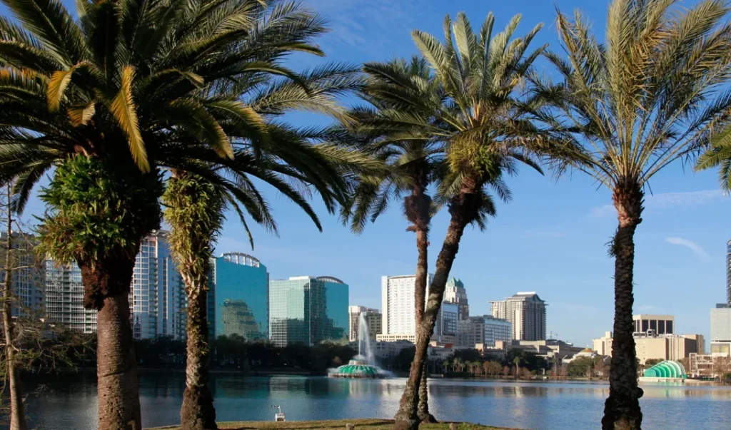 Palmeras a lo largo del Lake Eola con su fuente y el horizonte del centro de Orlando bajo el cielo azul