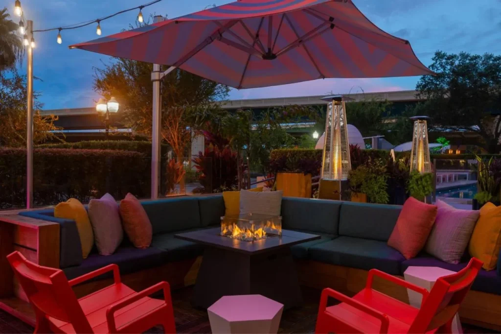 Mesa de fuego al aire libre con sofás acolchados y sillas rojas al atardecer en el Aloft Orlando Downtown