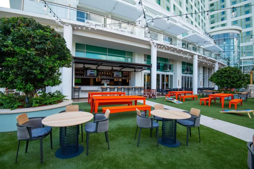Outdoor lawn terrace with tables and orange picnic benches by a bar at Hilton Orlando