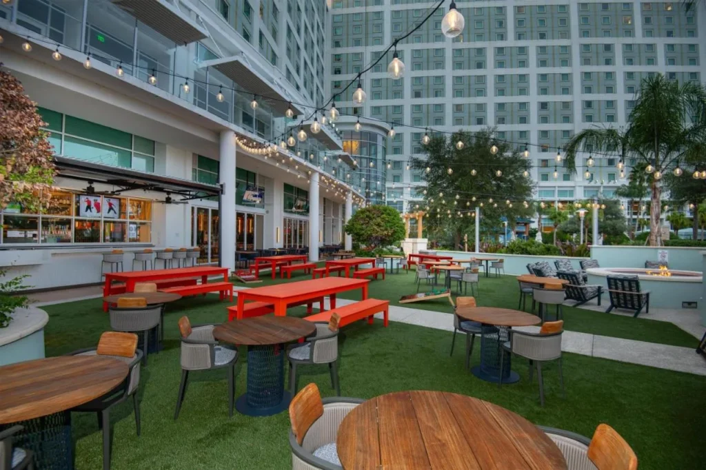 Outdoor lawn with bright orange picnic tables, string lights and a fire pit at Hilton Orlando
