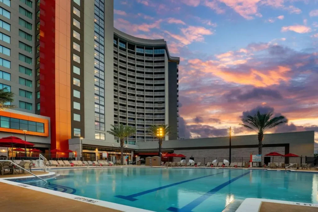 Piscina al aire libre al atardecer debajo de la torre curva del Drury Plaza Hotel Orlando Disney Springs