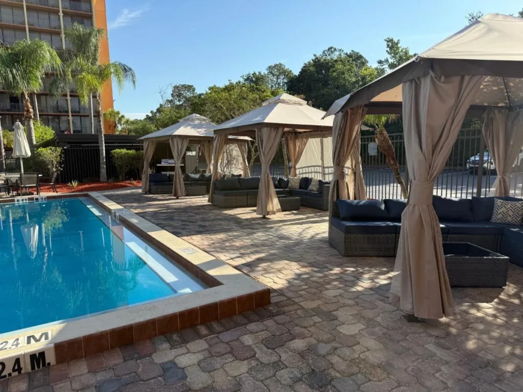 Piscina al aire libre junto a cabañas con cortinas y sofás lounge en Holiday Inn & Suites Orlando SW