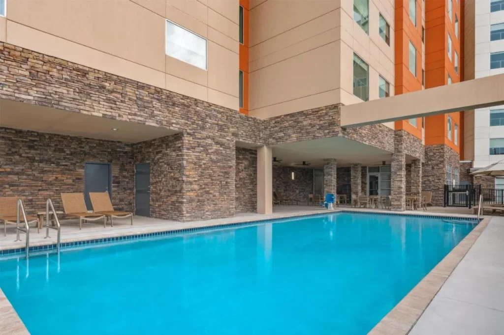 Piscina al aire libre junto a columnas y tumbonas revestidas de piedra en Hyatt House Orlando International Drive