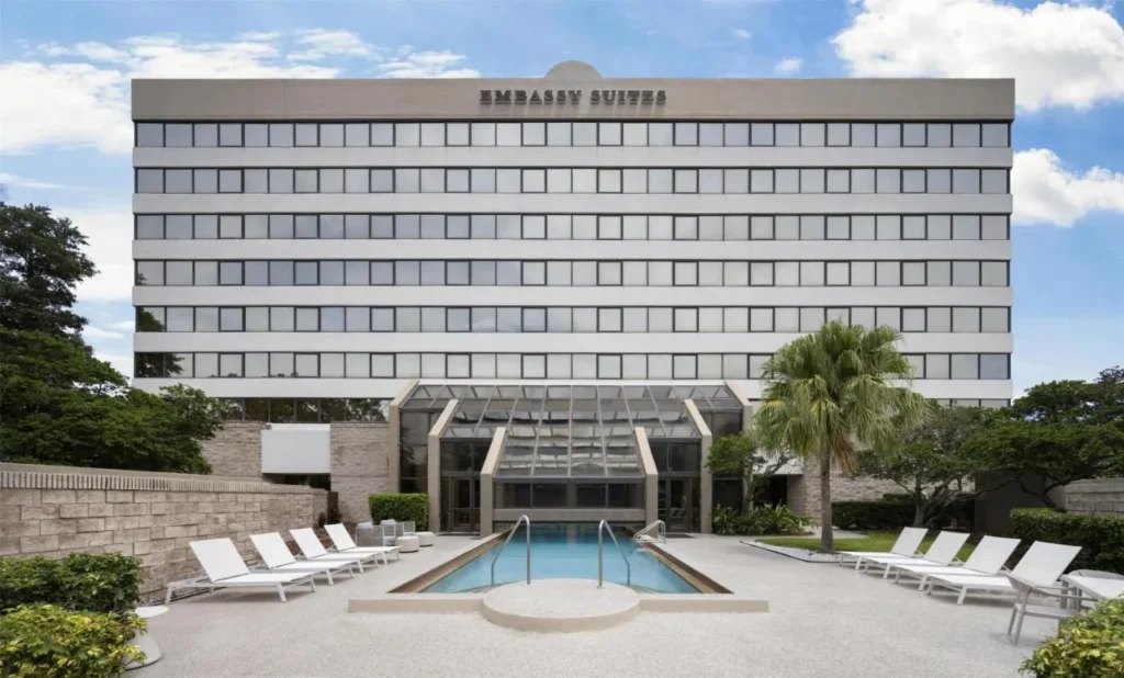 Cubierta de la piscina al aire libre con tumbonas que conducen a la piscina cubierta con techo de vidrio en Embassy Suites ICON Park