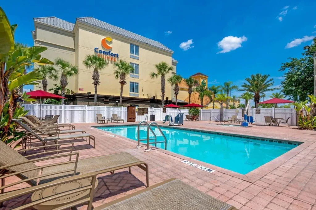 Outdoor pool, loungers and red umbrellas below Comfort Suites Near Universal Orlando Resort