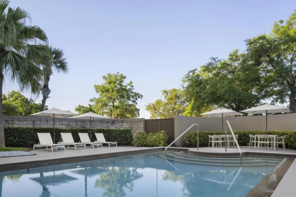 Piscina al aire libre, tumbonas y sombrillas bajo las palmas en Embassy Suites Orlando ICON Park
