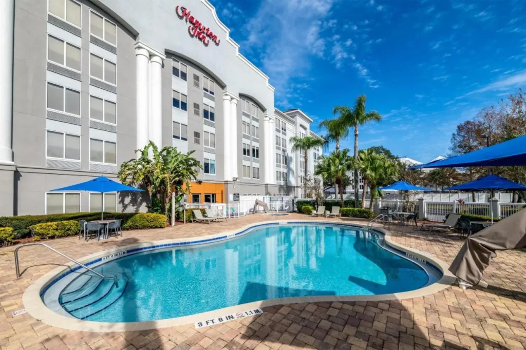 Piscina al aire libre con sombrillas azules junto al edificio Hampton Inn Orlando/Lake Buena Vista
