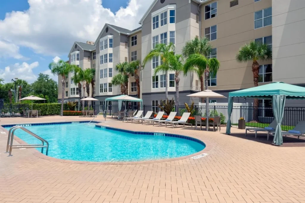 Piscina al aire libre con cabañas y tumbonas debajo de los edificios de la suite en Homewood Suites Nearest Universal