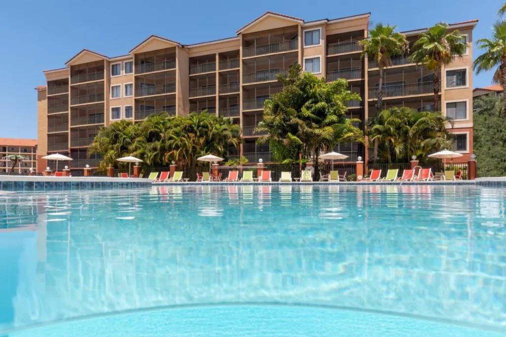 Outdoor pool with colorful loungers in front of a mid-rise villa building at Westgate Lakes