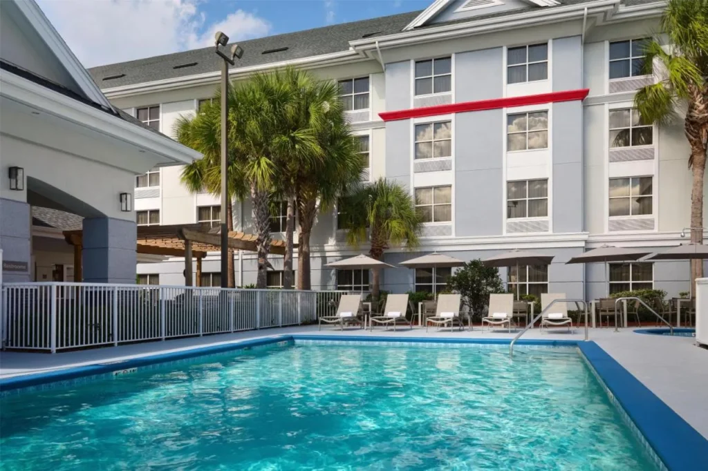 Piscina al aire libre con tumbonas y sombrillas junto al edificio del Homewood Suites Daytona Beach Speedway-Airport
