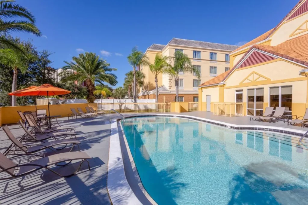 Piscina al aire libre con tumbonas al lado de los edificios amarillos del hotel La Quinta Orlando Universal área