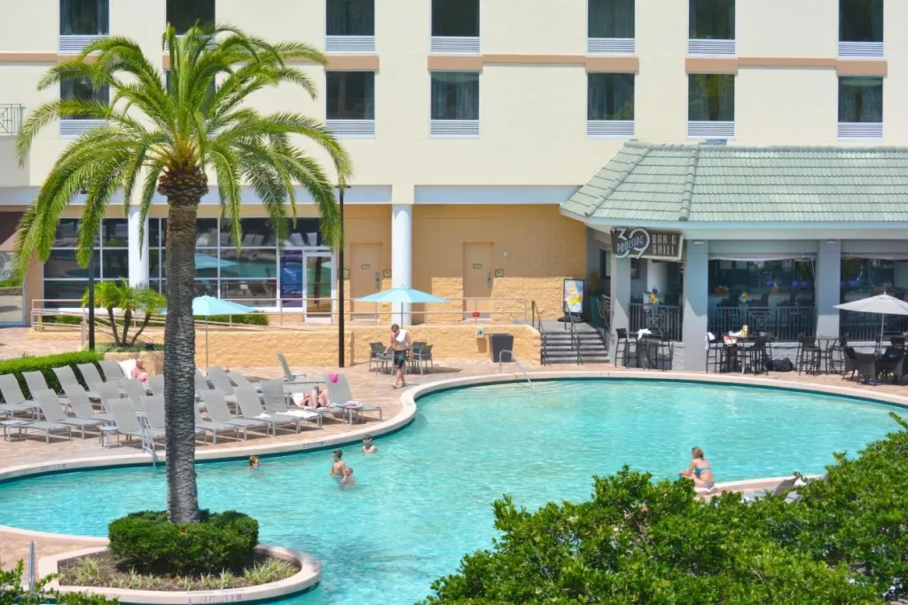 Outdoor pool with loungers, a palm island and '39 Poolside Bar and Grill, Rosen Plaza Hotel