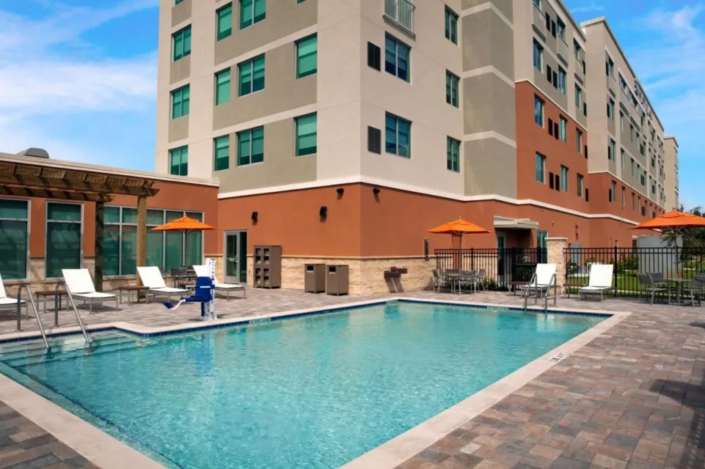 Outdoor pool with loungers and umbrellas beside Hyatt Place Titusville Kennedy Space Center building