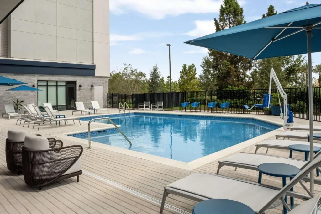 Piscina al aire libre con tumbonas, paraguas azules y sillas de mimbre en Home2 Suites Orlando Southeast Nona