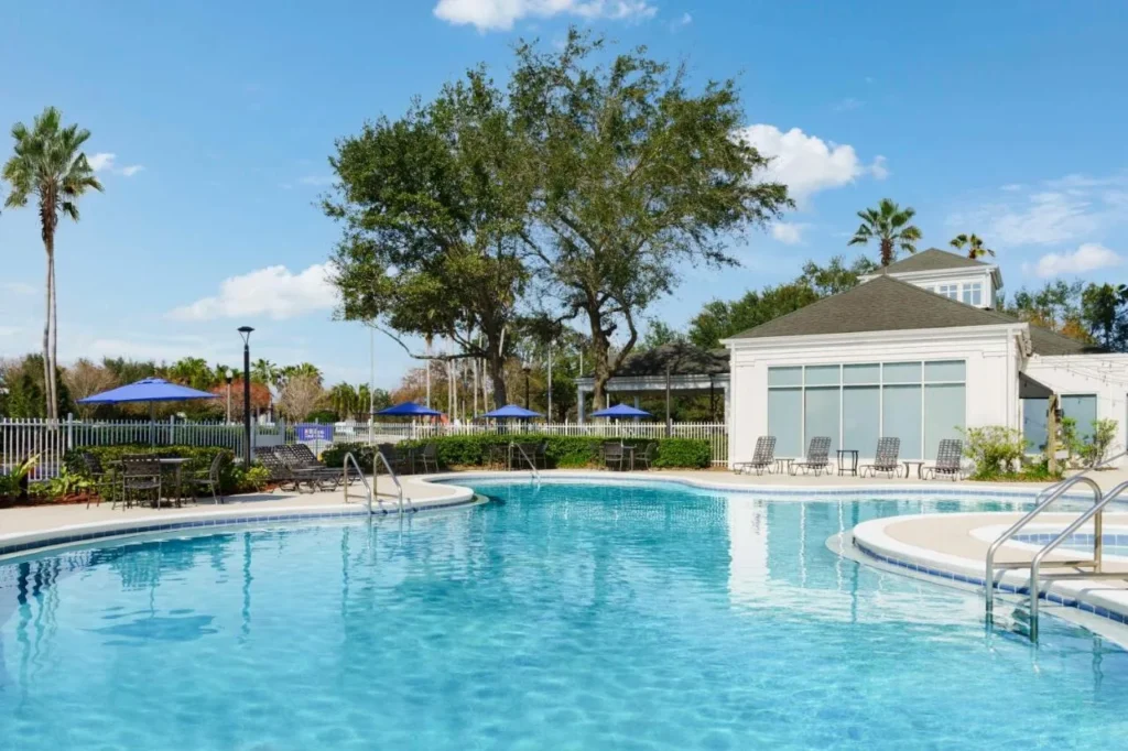 Piscina al aire libre con tumbonas, sombrillas y palmeras en Hilton Garden Inn Orlando at SeaWorld