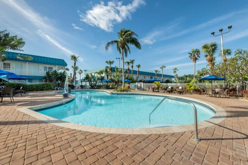 Outdoor pool with palm trees and blue umbrellas at Best Western Cocoa Beach - Port Canaveral